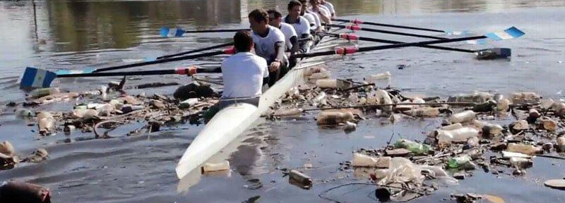 Imagen actual de remeros navegando en el Río Reconquista, con basura en la superficie del agua y las orillas.