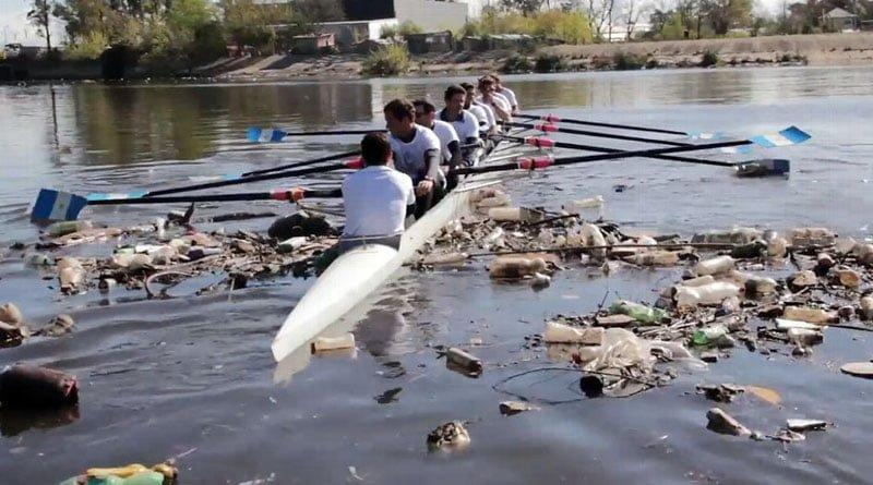 Imagen actual de remeros navegando en el Río Reconquista, con basura en la superficie del agua y las orillas.